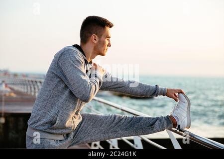 Jeune homme séduisant dans le sportswear , faisant des exercices d'entraînement pour les jambes, sur le quai, à l'extérieur. Banque D'Images