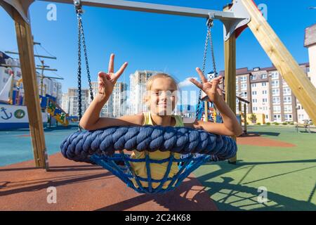 La jeune fille montre avec joie la lettre 'V' par les doigts sur les deux mains, faire de la série swing swing Banque D'Images
