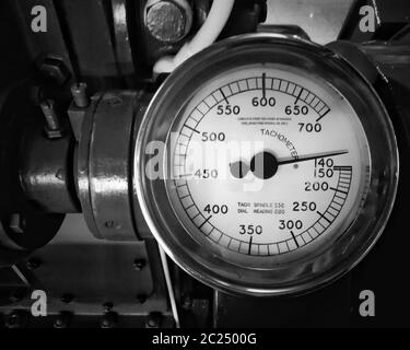 image monochrome d'un grand tachymètre en métal ancien avec un indicateur rond avec le cadran marqué de numéros montés sur un gros moteur Banque D'Images