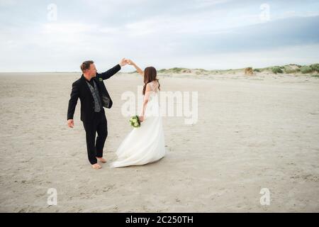 Des jeunes mariés dansent sur une plage de sable. Mariée et marié regardant l'un à l'autre et souriant. Danse pieds nus. Concept de mariage. Banque D'Images