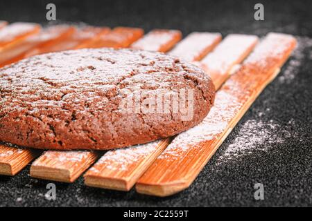 biscuits au chocolat et à l'avoine parsemés de sucre en poudre se trouve sur une plaque de bambou sur béton noir Banque D'Images