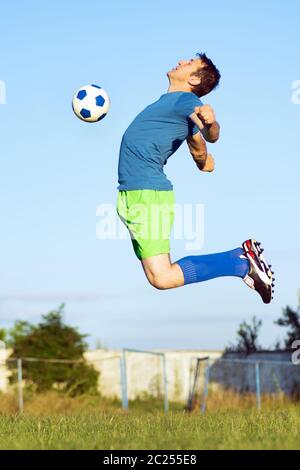 Le joueur de football saute à frapper le ballon de football avec la poitrine, sport action en mouvement. Banque D'Images