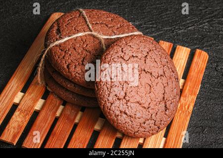 les biscuits de flocons d'avoine au chocolat, attachés avec une corde, reposent sur une plaque de bambou sur du béton noir Banque D'Images