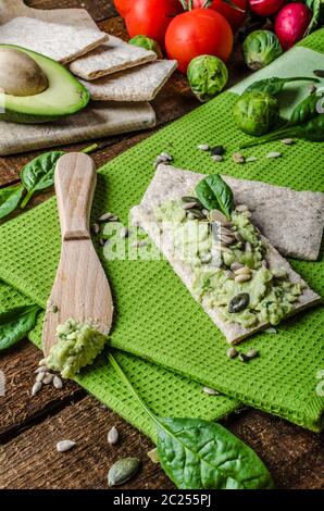 Accueil avocat propagation sur des biscottes avec graines de tournesol et de citrouille, de sésame et d'herbes épinards Banque D'Images