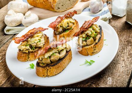 Petit-déjeuner rustique - ail rôties, poêlée de champignons, oeufs brouillés et bacon sur le dessus Banque D'Images