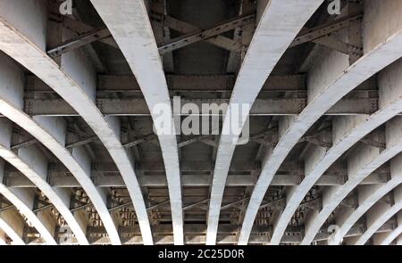 vue en perspective des poutres en acier incurvées en forme d'arc sous un ancien pont routier avec rivets et jambes de force peints en gris Banque D'Images