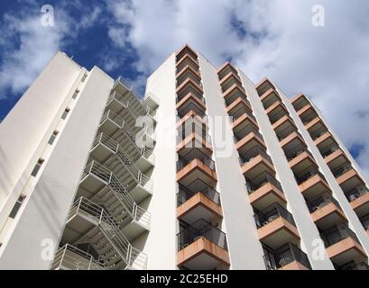 vue en angle sur un ancien immeuble d'appartements en béton blanc des années 1960 avec marches et balcons contre ciel bleu et nuages Banque D'Images