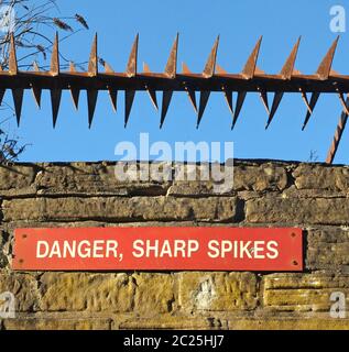 fer rouillé pointes pointues sur le dessus d'un vieux mur en pierre avec un signe de danger rouge contre un ciel bleu Banque D'Images