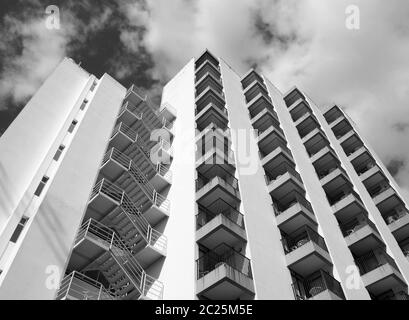 vue en angle monochrome d'un ancien immeuble d'appartements en béton blanc des années 1960 avec marches et balcons contre le ciel et les nuages Banque D'Images