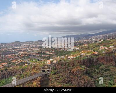 vue aérienne sur le paysage du pont autoroutier de funchal, qui pénètre dans un tunnel dans la vallée avec des bâtiments et des rues du cit Banque D'Images