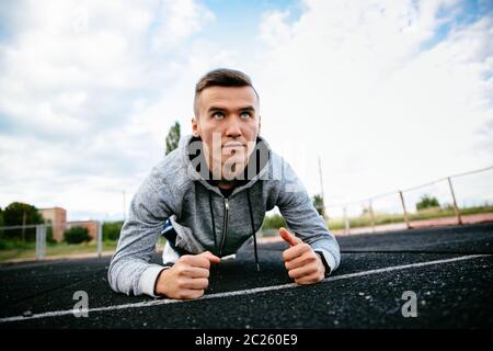 Jeune homme sportif en position de planche sur les coudes avec concentration face au stade. Banque D'Images