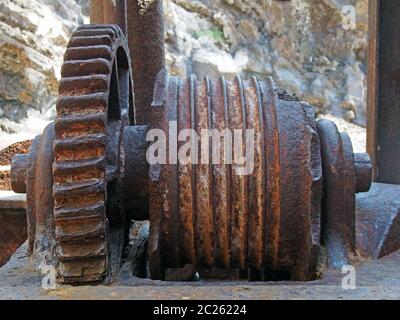 gros plan de machines cassées rouillées anciennes avec roue dentée et roue de treuil contre un mur en pierre Banque D'Images