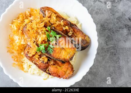 Tranches de poisson Panga frits à l'ail, servi avec du riz brun. Banque D'Images