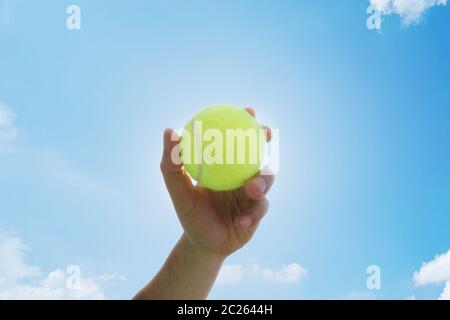 Homme tenant et servant un tennisball jaune contre le ciel bleu. Sports Banque D'Images