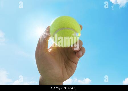 Homme tenant et servant un tennisball jaune contre le ciel bleu. Sports Banque D'Images