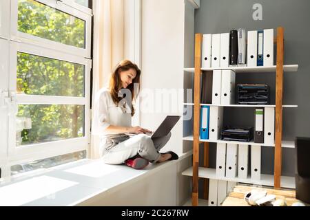 Vue latérale d'Happy Young Businesswoman Working On Laptop In Office Banque D'Images