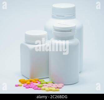 Comprimés colorés avec flacons blancs fermés sur fond blanc avec étiquette vierge. Industrie pharmaceutique. Interaction médicamenteuse. Antécédents de la pharmacie. Banque D'Images