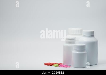 Comprimés roses, verts et rouges sur fond blanc avec contenant pour flacon de médicament. Emballage résistant à la lumière. Industrie pharmaceutique. Vitamine et supplemente Banque D'Images