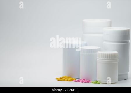 Comprimés jaunes, roses et verts sur fond blanc avec contenant pour flacon de médicament. Emballage résistant à la lumière. Industrie pharmaceutique. Vitamine et souple Banque D'Images