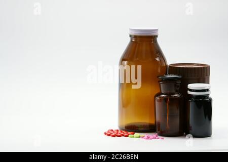 Comprimés roses, verts et rouges sur fond blanc avec contenant de bouteille de médicament ambre. Emballage résistant à la lumière. Industrie pharmaceutique. Vitamine et sup Banque D'Images