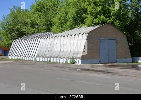 Hangar industriel avec murs en aluminium et supports de toit sur une fondation en béton près des arbres verts Banque D'Images