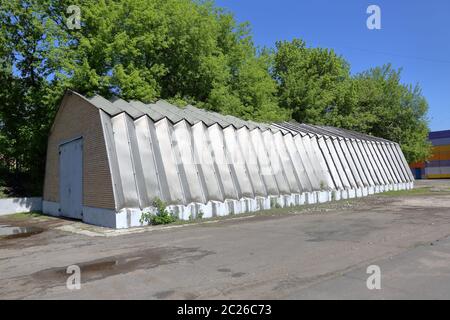 Hangar industriel avec murs en aluminium et supports de toit sur une fondation en béton près des arbres verts Banque D'Images