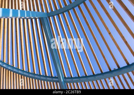 Construction semi-circulaire architecturale d'un cadre en métal bleu, déjà légèrement rouillé et de lamelles en bois à conception ouverte Banque D'Images