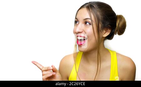 Portrait de gaie rire fille avec deux chingnon pointant par le doigt sur le côté. Belle femme en jaune réservoir haut surpris regardant côté montrer Banque D'Images