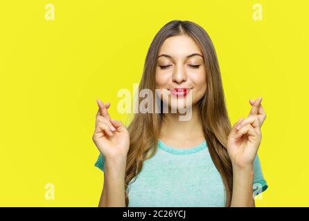 Une fille positive et charmante portant un t-shirt bleu azur exprimant son enthousiasme tout en faisant avec ou en espérant quelque chose avec des mains levées et des doigts croisés Banque D'Images