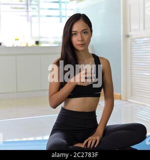 Vue rapprochée d'une femme portant des vêtements d'exercice tenant un verre d'eau et assise sur un tapis de yoga Banque D'Images