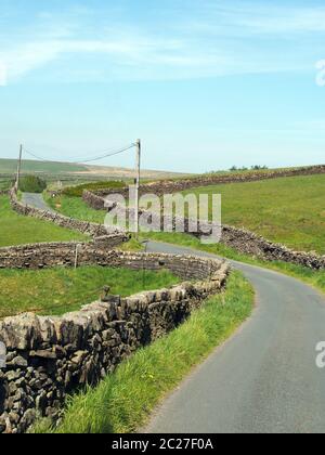 un carrefour sur une ruelle étroite sinueuse de campagne bordée par des murs de pierre sèche dans la campagne vallonnée du yorkshire dales avec bleu été sk Banque D'Images