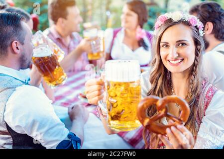 Femme qui se laque à la caméra avec un verre de bière dans un pub bavarois tenant le bretzel à la main Banque D'Images