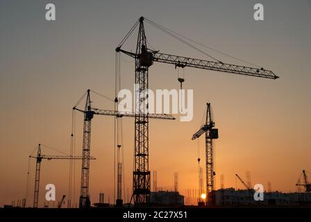 Paysage industriel avec des silhouettes de grues sur le fond coucher de soleil Banque D'Images