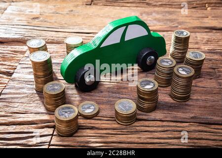 Voiture en bois verte près de la pile de pièces sur un bureau en bois Banque D'Images