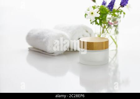 Serviettes à côté d'un pot crème devant un fond blanc et fleurs dans un vase. Banque D'Images