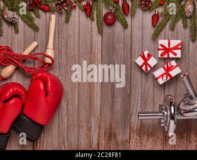 Haltères, gants de boxe, boîtes-cadeaux, branches de sapin et décoration de Noël sur fond de bois. Vue de dessus avec espace de copie. Nouvel an, Noël. Fitness Banque D'Images