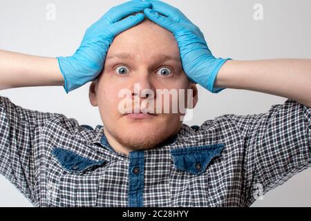 un jeune homme en gants madicine bleus a une panique des émotions tiennent sur la tête. concept du coronavirus. pandémie Banque D'Images