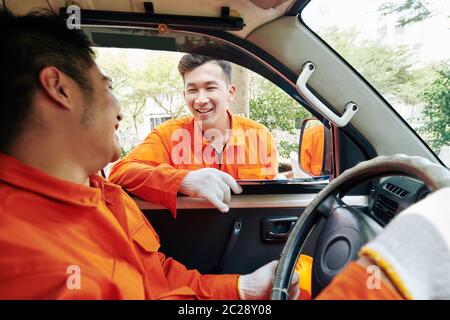 Homme asiatique portant des vêtements orange assis en voiture parlant avec son collègue debout à l'extérieur, photo horizontale Banque D'Images