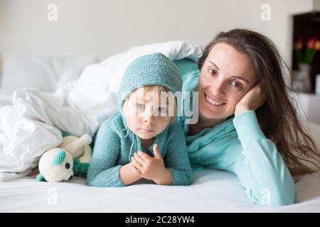 Bonne mère et enfant, garçon, avec une tenue assortie, allongé dans le lit, souriant heureux, embrassant et se cachant sous la couverture Banque D'Images