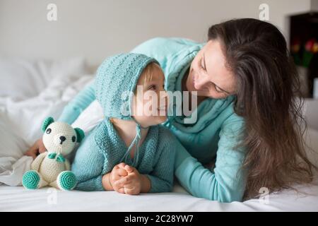 Bonne mère et enfant, garçon, avec une tenue assortie, allongé dans le lit, souriant heureux, embrassant et se cachant sous la couverture Banque D'Images