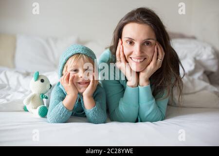 Bonne mère et enfant, garçon, avec une tenue assortie, allongé dans le lit, souriant heureux, embrassant et se cachant sous la couverture Banque D'Images