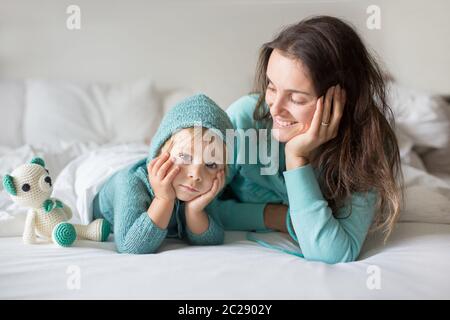 Bonne mère et enfant, garçon, avec une tenue assortie, allongé dans le lit, souriant heureux, embrassant et se cachant sous la couverture Banque D'Images