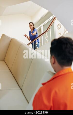 Hommes en mouvement portant un grand canapé à l'étage, femme mûre debout là les dirigeant, plan vertical sur l'épaule Banque D'Images