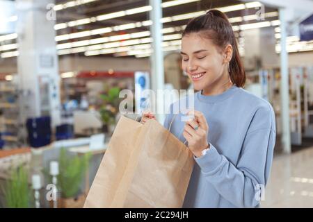 Jeune femme attrayante qui a l'air excitée, ouvrant son sac de shopping. Une cliente heureuse regarde à l'intérieur de son sac Banque D'Images