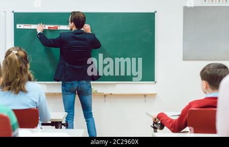 Des élèves attentifs regardent le professeur dessiner au tableau noir en classe Banque D'Images