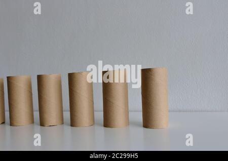 Attention sélective sur la première rangée de rouleaux de papier toilette vides debout sur une table en bois contre un mur de ciment blanc sous la lumière du soleil Banque D'Images