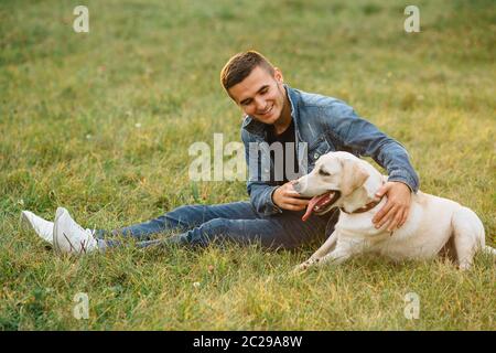 Smiling man sitting on grass avec son chien labrador in park Banque D'Images