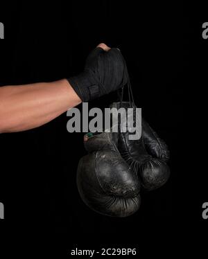 Le bras de l'homme enveloppé dans un bandage élastique noir sports détient old vintage paire de gants de boxe en cuir, fond noir, copy space Banque D'Images