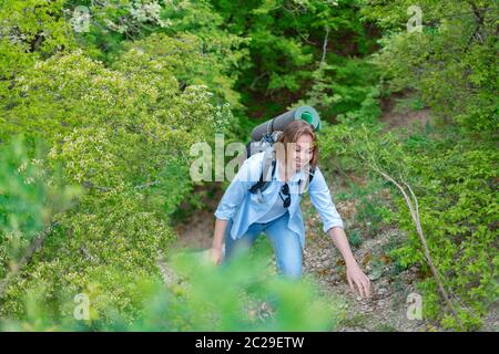 Femme souriante grimpant sur un sentier de montagne. Plantes et arbres en arrière-plan. Sports et tourisme actifs. Banque D'Images