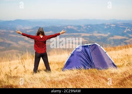 Vue arrière de la femme randonnée sentier de montagne, debout près de la tente avec les mains vers le haut, appréciant matin d'été dans les montagnes Carpathian. Camping aventure vacatio Banque D'Images